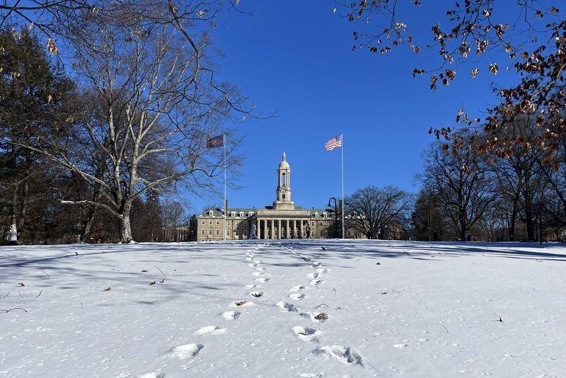 A faraway picture of Old Main with a blue sky behind it and several paths of footprints in the snow leading to it